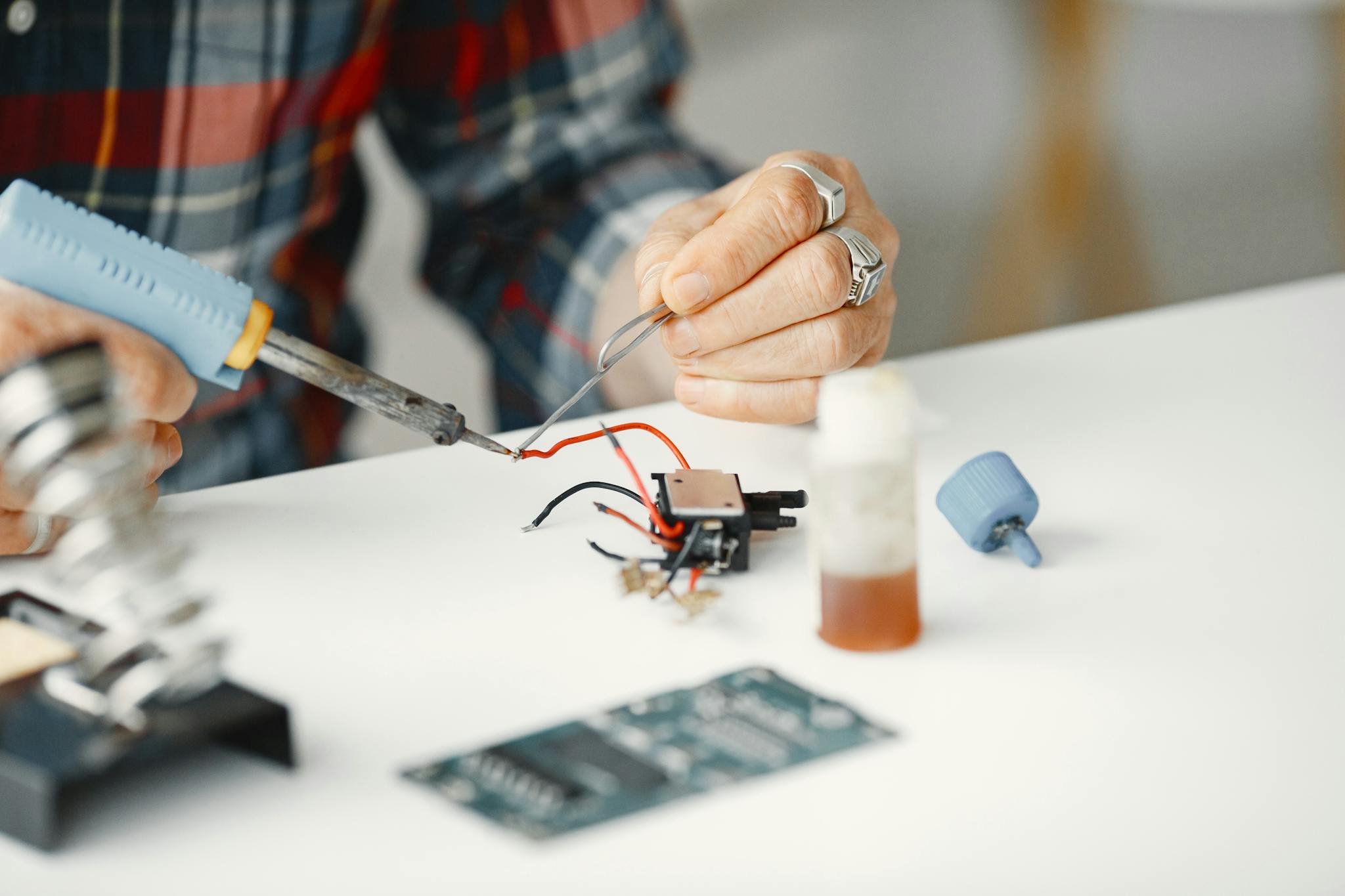 Detailed close-up of hands soldering electronic components with a soldering iron on a table.
